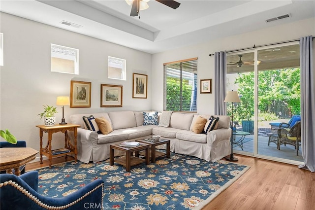 living room featuring visible vents, a tray ceiling, ceiling fan, and wood finished floors