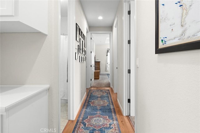hallway featuring baseboards, light wood finished floors, and recessed lighting