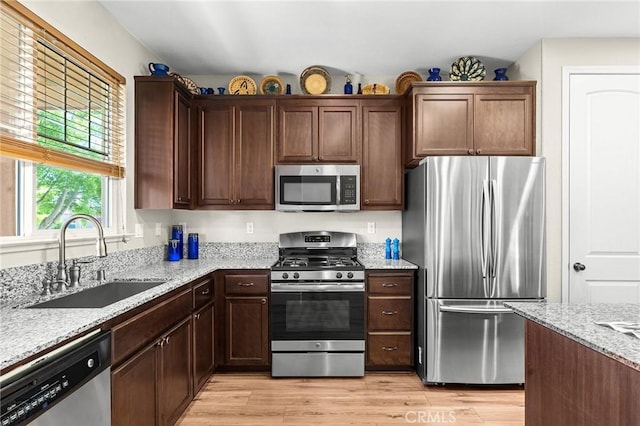 kitchen with light wood finished floors, appliances with stainless steel finishes, light stone countertops, and a sink