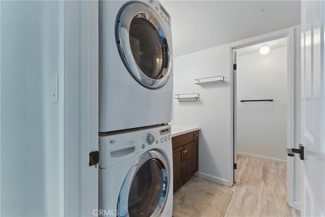 washroom featuring baseboards, stacked washer and dryer, light wood-style flooring, and cabinet space
