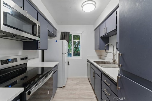 kitchen with light wood finished floors, a sink, stainless steel appliances, baseboards, and light countertops