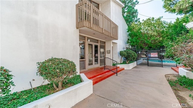 property entrance featuring fence, french doors, a community pool, a balcony, and stucco siding