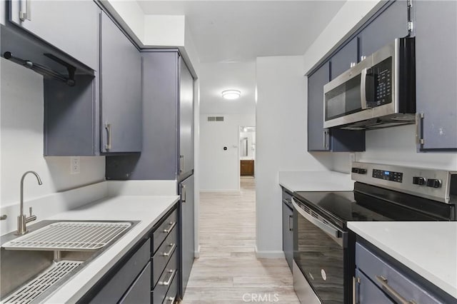 kitchen featuring light wood finished floors, light countertops, appliances with stainless steel finishes, and a sink
