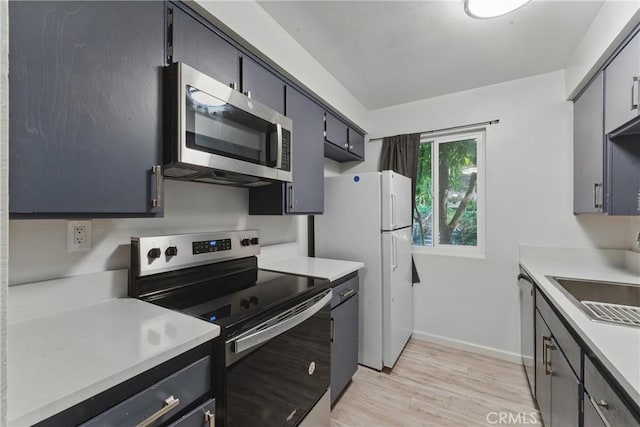 kitchen featuring baseboards, light countertops, stainless steel appliances, and light wood-style flooring