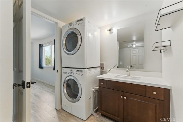 laundry area featuring light wood finished floors, a sink, stacked washer and dryer, laundry area, and baseboards
