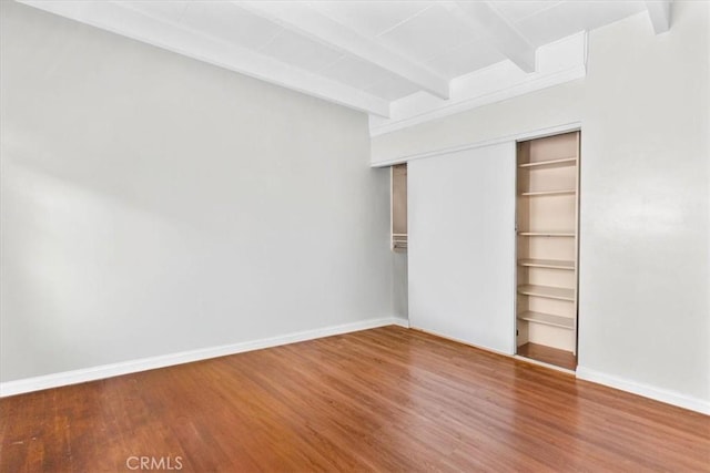 unfurnished bedroom featuring a closet, wood finished floors, baseboards, and beamed ceiling