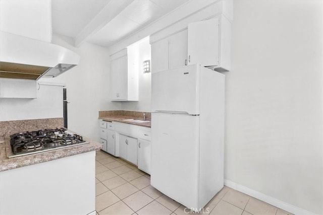 kitchen with freestanding refrigerator, stainless steel gas cooktop, light tile patterned floors, white cabinetry, and wall chimney range hood