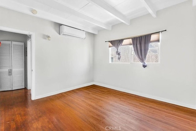 unfurnished room featuring baseboards, beamed ceiling, a wall unit AC, and wood finished floors