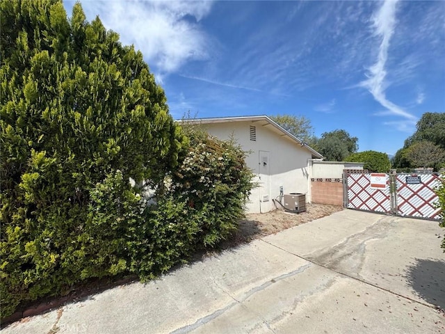 view of home's exterior with central air condition unit, stucco siding, fence, and a gate