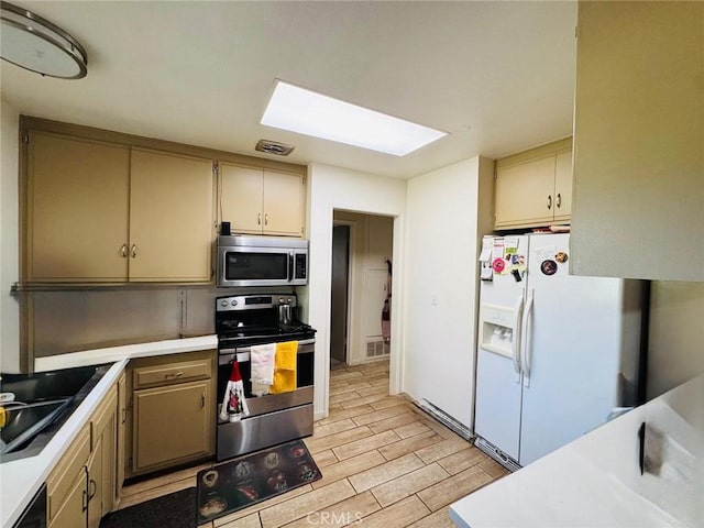 kitchen featuring stainless steel appliances, a sink, light wood-style floors, light countertops, and a skylight