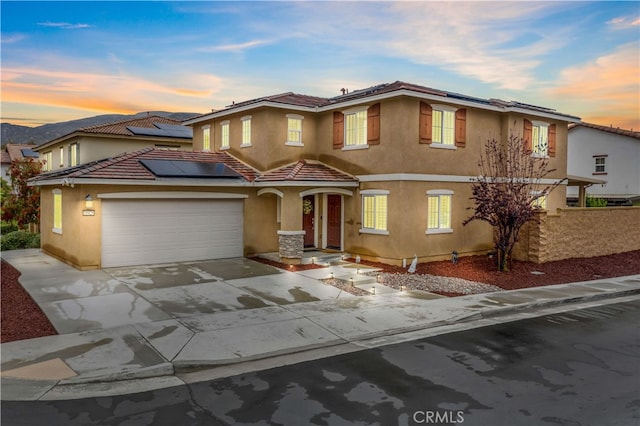 traditional home featuring a tile roof, roof mounted solar panels, concrete driveway, and stucco siding