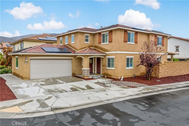 traditional-style house with roof mounted solar panels, stucco siding, a tile roof, fence, and concrete driveway