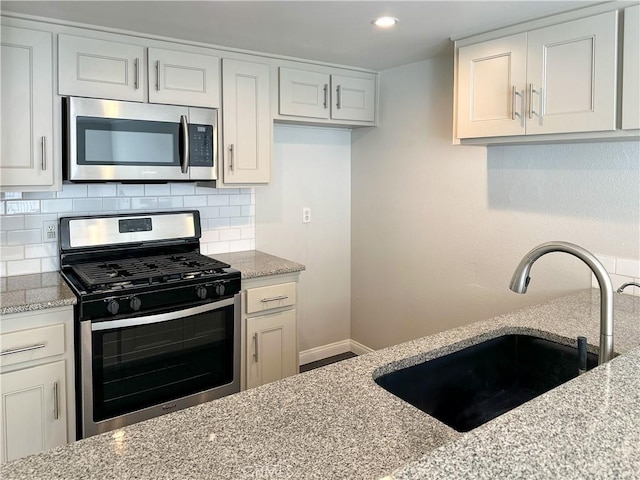 kitchen featuring backsplash, light stone countertops, appliances with stainless steel finishes, and a sink