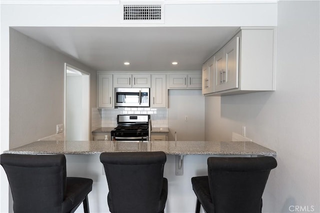 kitchen with a peninsula, appliances with stainless steel finishes, visible vents, and tasteful backsplash