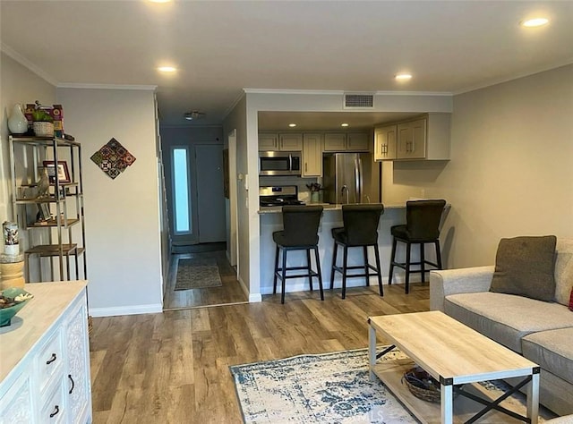 living area featuring wood finished floors, ornamental molding, visible vents, recessed lighting, and baseboards