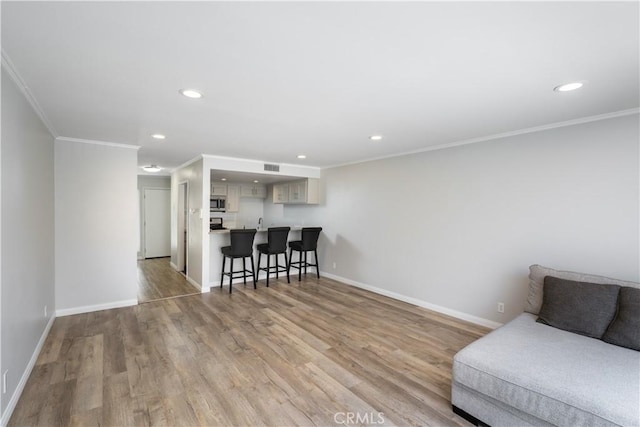 living room featuring light wood finished floors, crown molding, baseboards, and recessed lighting