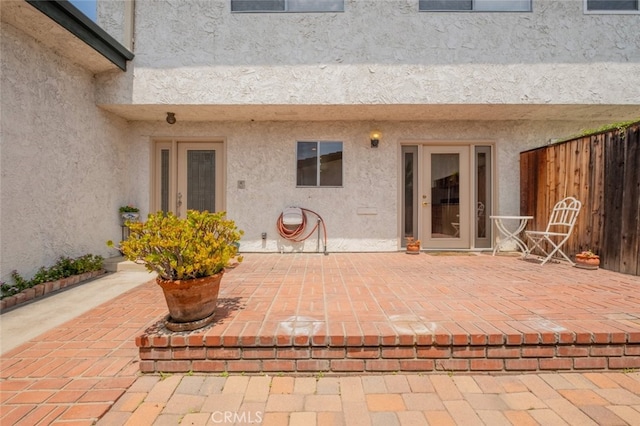 view of exterior entry featuring a patio area, stucco siding, and fence