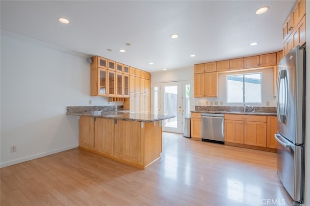 kitchen with a peninsula, appliances with stainless steel finishes, glass insert cabinets, and light wood finished floors