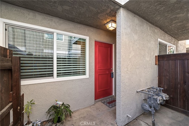 doorway to property featuring stucco siding and fence