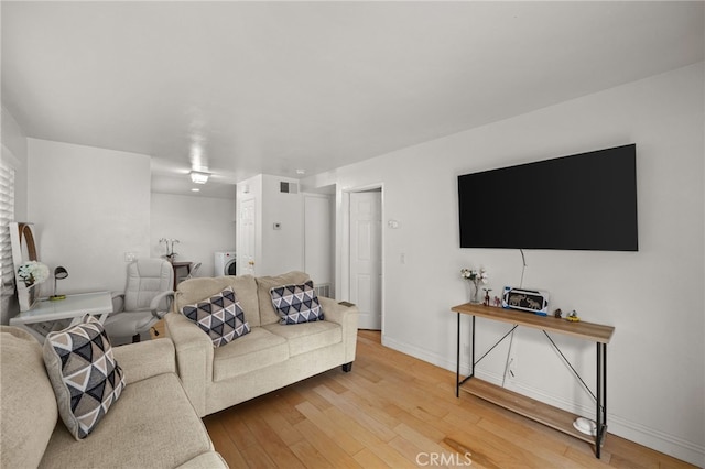 living room featuring washer / dryer, visible vents, wood finished floors, and baseboards