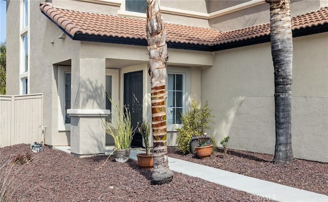 doorway to property with a tiled roof, stucco siding, and fence