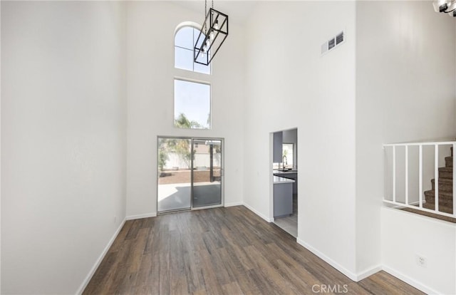 unfurnished living room featuring baseboards, visible vents, wood finished floors, and a towering ceiling