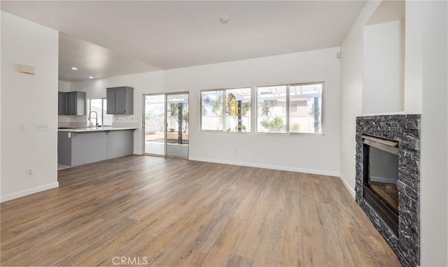 unfurnished living room featuring baseboards, light wood-style floors, and a glass covered fireplace