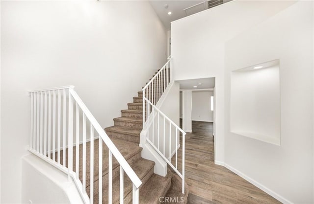 stairway featuring baseboards, recessed lighting, a high ceiling, and wood finished floors