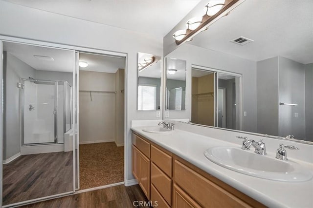 13167 Hollister St, Hesperia, CA 92344 - bathroom featuring wood finished floors, double vanity, a stall shower, a walk in closet, and baseboards