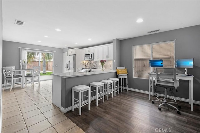 kitchen with a breakfast bar, appliances with stainless steel finishes, white cabinets, and visible vents
