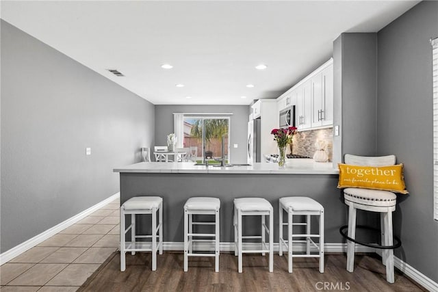 kitchen with a peninsula, white cabinetry, visible vents, stainless steel microwave, and fridge