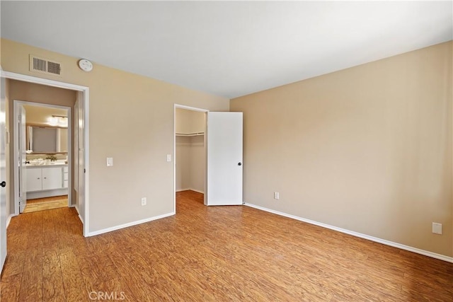 unfurnished bedroom featuring baseboards, a spacious closet, visible vents, and wood finished floors