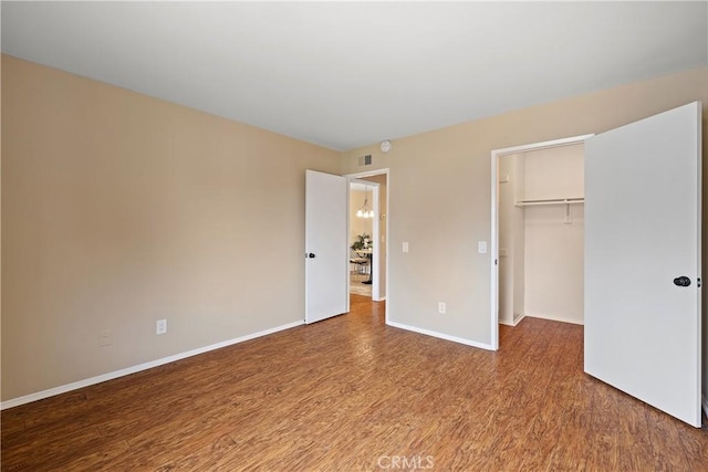unfurnished bedroom with a closet, baseboards, visible vents, wood finished floors, and a spacious closet