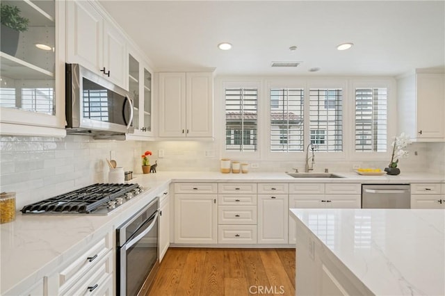 kitchen featuring light wood-style flooring, a sink, stainless steel appliances, visible vents, and backsplash