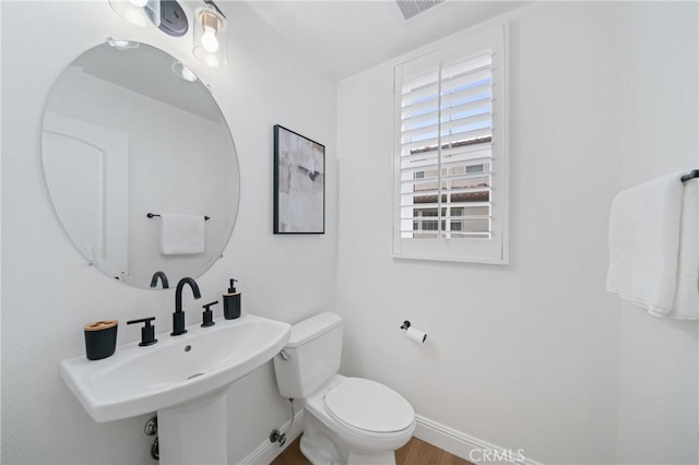 half bathroom with a sink, toilet, wood finished floors, visible vents, and baseboards