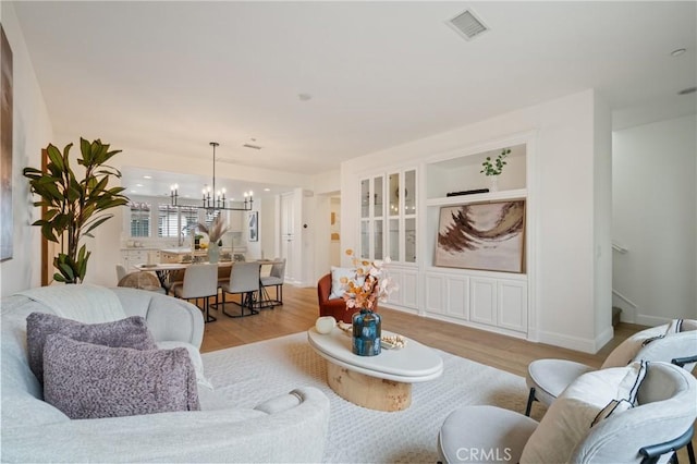 living room featuring stairway, an inviting chandelier, light wood finished floors, and visible vents