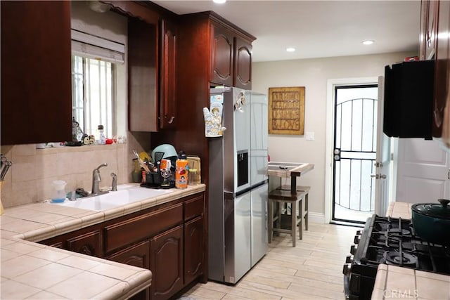 kitchen with a sink, backsplash, tile countertops, and stainless steel refrigerator with ice dispenser