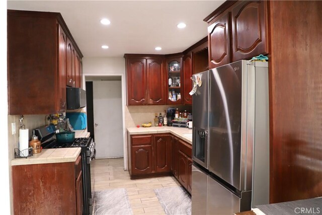 kitchen featuring tile countertops, stainless steel refrigerator with ice dispenser, black microwave, glass insert cabinets, and gas range oven