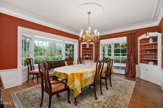 dining room with wood finished floors, built in shelves, a chandelier, crown molding, and plenty of natural light