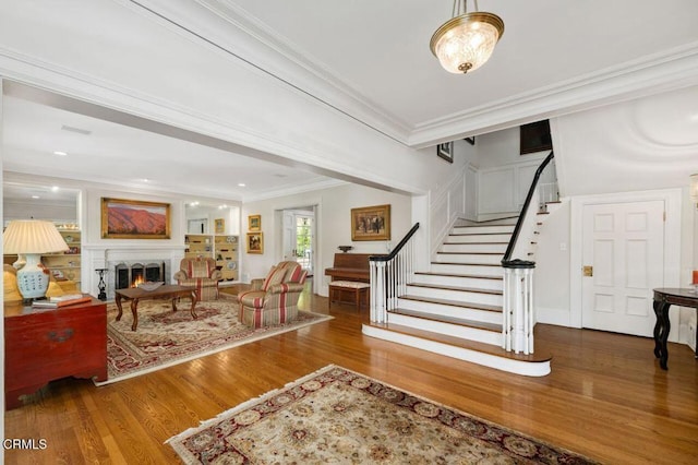 entrance foyer with stairway, crown molding, a warm lit fireplace, and wood finished floors