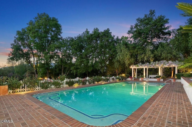 pool at dusk with a patio, a pergola, and an outdoor pool
