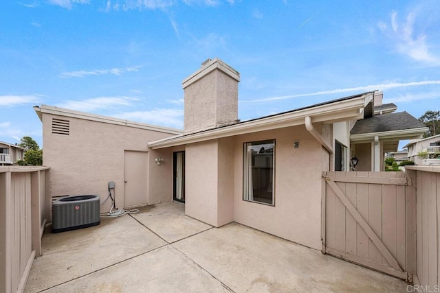 back of property featuring a gate, a patio, stucco siding, a chimney, and central AC unit