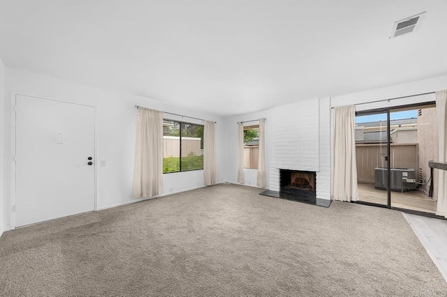 unfurnished living room featuring light carpet, a brick fireplace, visible vents, and plenty of natural light
