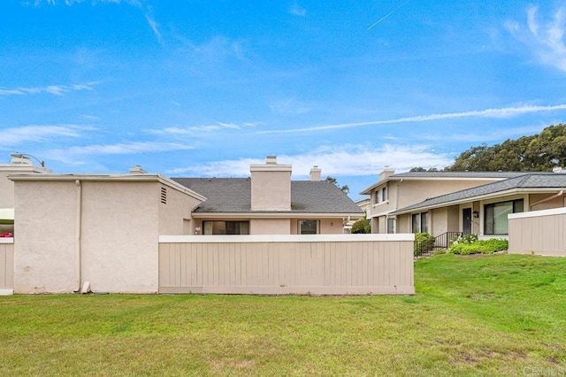 back of property featuring a lawn, stucco siding, and fence