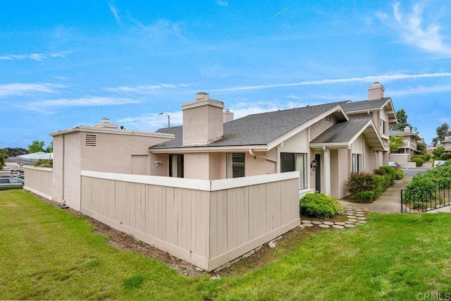 rear view of house featuring roof with shingles, fence, a chimney, and a lawn