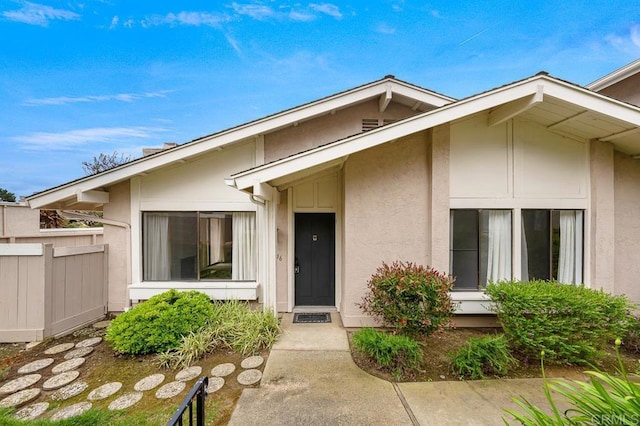 entrance to property featuring fence and stucco siding
