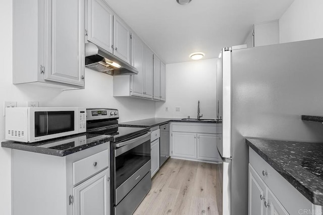 kitchen with light wood finished floors, a sink, dark stone counters, stainless steel appliances, and under cabinet range hood