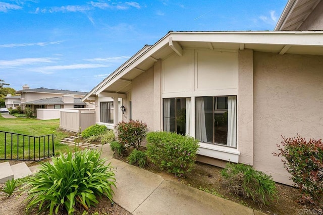 view of exterior entry featuring a lawn, stucco siding, and fence