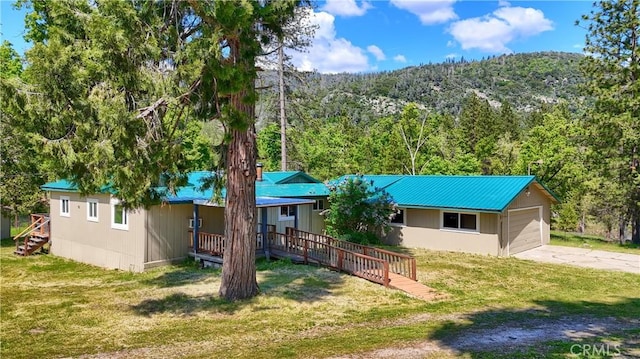 ranch-style house featuring driveway, a forest view, a front lawn, and metal roof