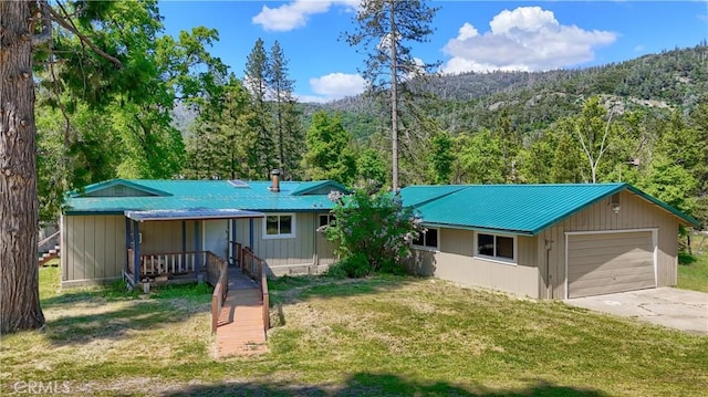 ranch-style house with a porch, driveway, a view of trees, a front yard, and metal roof